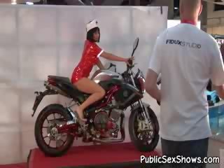 Luscious busty brunette dressed like nurse posing on bike at strip show